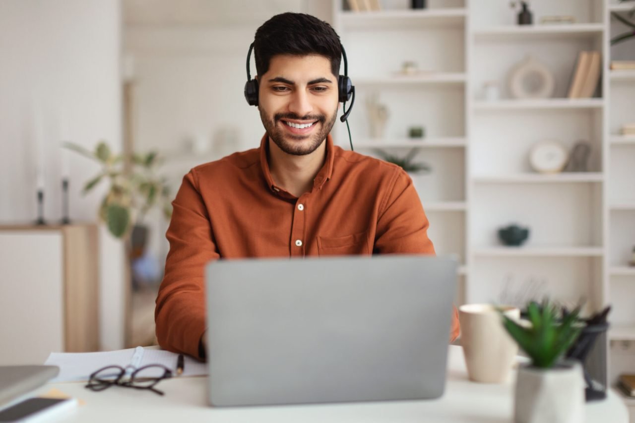 Arab Man Using Laptop Wearing Headset Sitting At Desk E1698767765625.jpg